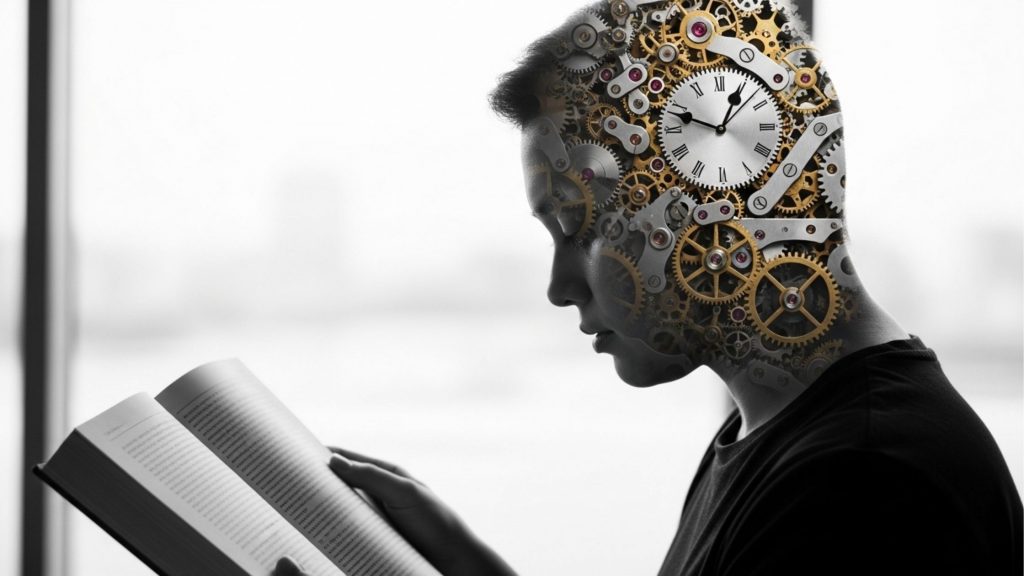 Imagem artística em preto e branco do perfil de uma pessoa lendo um livro. A parte superior da cabeça é transparente, revelando um mecanismo complexo de engrenagens douradas e prateadas de relógio, simbolizando o funcionamento da mente, a disciplina e o tempo dedicado ao aprendizado.