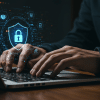 Pessoa digitando em um laptop com ícones digitais de segurança cibernética e um cadeado iluminado no centro, representando proteção de dados e privacidade online.