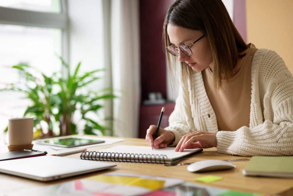 Pessoa estudando e anotando informações sobre as formas de provimento de cargos públicos, com livros e material de escritório sobre a mesa.