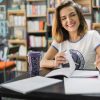 Mulher sorrindo enquanto estuda, ela está em uma biblioteca